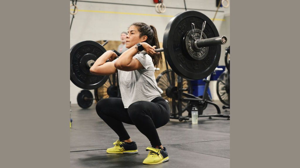 En kvinnlig Styrkelyftare som lyfter en skivstång med vikt. Övningen hon utför är en frontsquat.